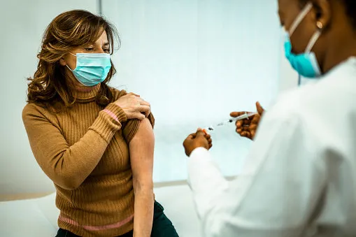 female african american doctor giving flu or covid19 vaccine to a middle-aged woman wearing protective face masks vaccination and prevention against virus pandemic