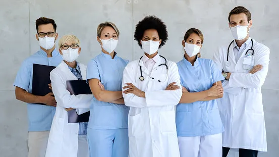 group of healthcare workers wearing protective face masks while standing with arms crossed and looking at camera