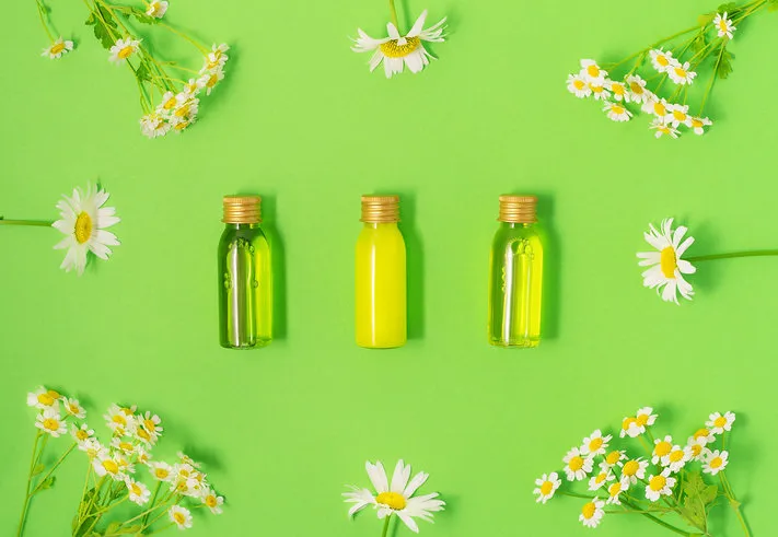 flat lay of small mockup bottles with spa cosmetic products on green background with fresh camomile blossoms women beauty and beauty salon cosmetics concept eco concept
