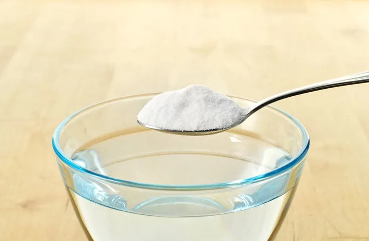 close-up of baking soda on spoon against background of glass of water on wooden table bicarbonate of soda copy space