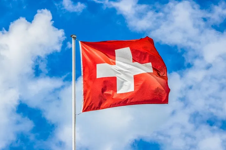 classic view of the national flag of switzerland waving in the wind against blue sky and clouds on a sunny day in summer on the first of august, the national holiday of the swiss confederation