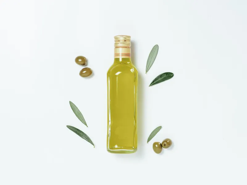 olive oil glass bottle mock up top view of clear glass bottle with olive oil on white background with green olives and fresh green olive tree leaves copy space