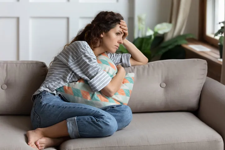 frustrated young lady sitting on sofa, cuddling pillow, looking away at window lost in thoughts unhappy stressed millennial woman regretting of wrong decision, spending time alone in living room