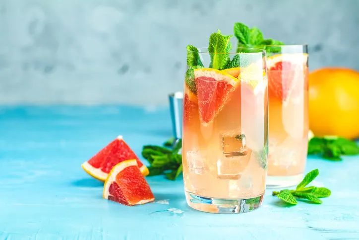 grapefruit and mint gin tonic cocktail, refreshing drink with ice cold summer citrus refreshing drink cocktail or beverage with ice on blue concrete surface