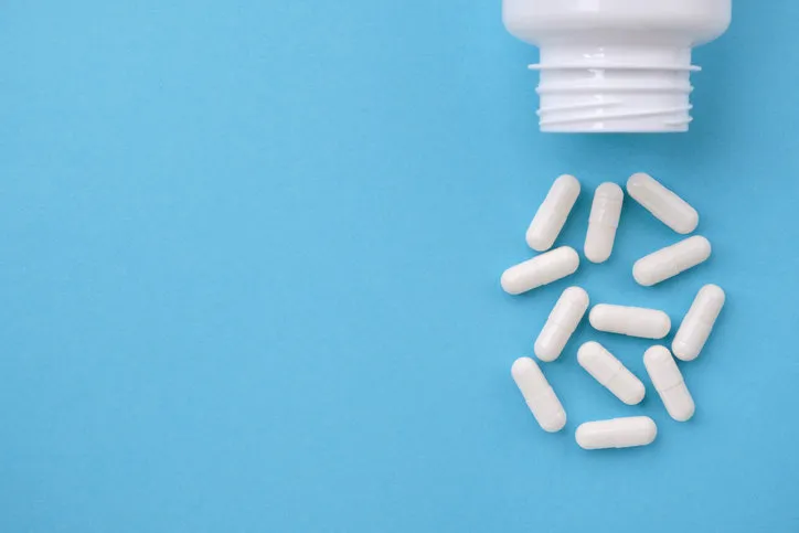 white capsules falling from the white bottle on blue paper background concept of pharmacy