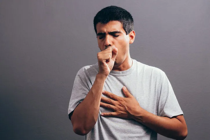 man coughing into his fist, isolated on a gray background