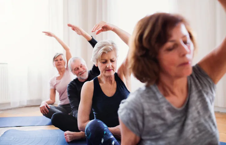 group of active senior people doing yoga exercise in community center club