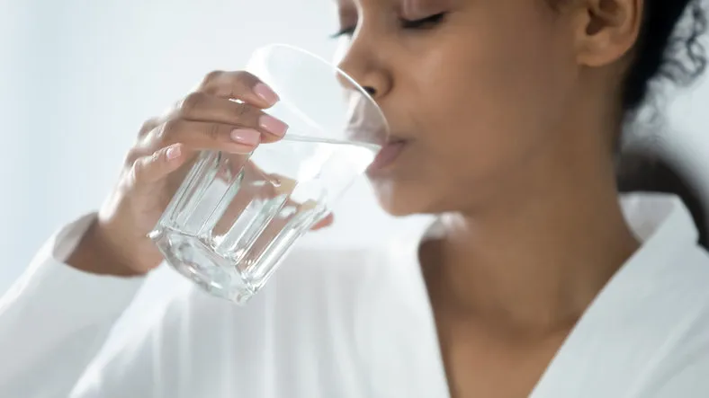 close up beautiful african woman holding glass drinking a pill with still water minerals and vitamins for female, dietary supplement, reducing of thirst, body water balance healthy lifestyle concept