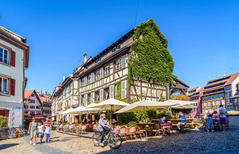 strasbourg, france - september 15, 2019  the sidewalk restaurant au pont saint-martin, set in a half-timbered house in the petite france quarter, with tourists strolling and a cyclist passing by