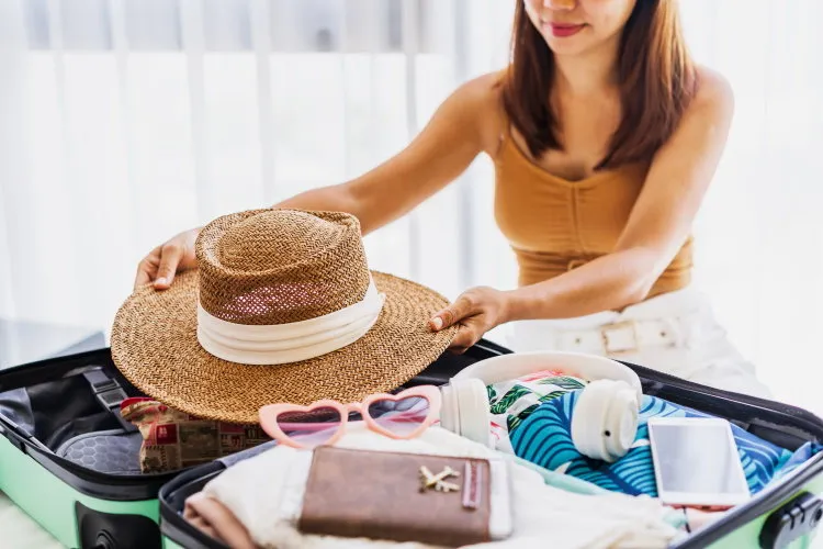 young woman traveler sitting on the bed packing her suitcase preparing for travel on summer vacation