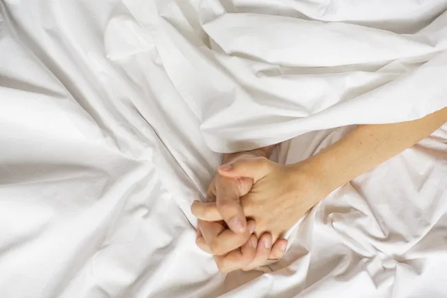 sensual beautiful young couple is having sex on bed female hand pulling white sheets in ecstasy, orgasm love concept wellness couple in love orgasm concept