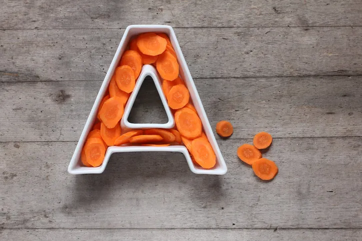 vitamin a in food concept plate in the shape of the letter a with sliced fresh carrots on wooden background flat lay or top view