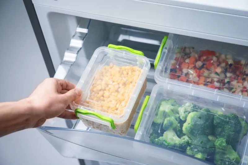 woman taking container with frozen corn from refrigerator
