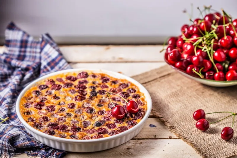 cherry french pie in a round plate on a wooden table with a napkin plate with sweet cherries on the background is blurred