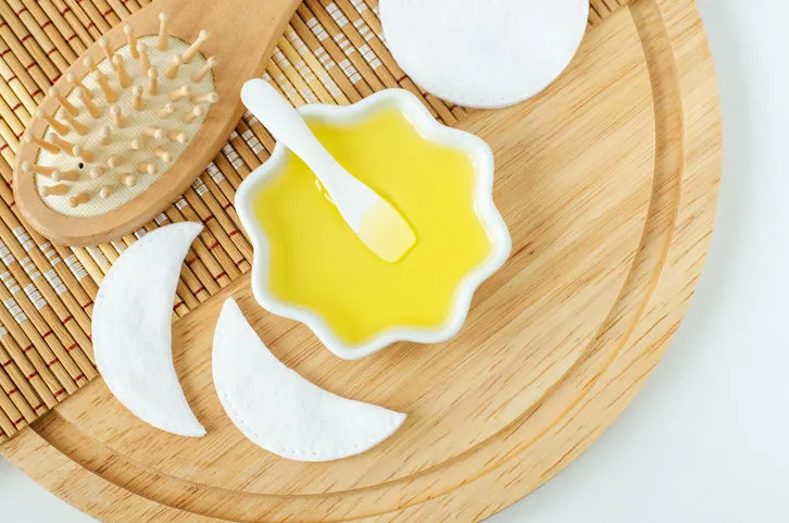 small white bowl with cosmetic (massage, cleansing) oil and wooden hairbrush natural haircare, spa and beauty treatment recipe top view, copy space