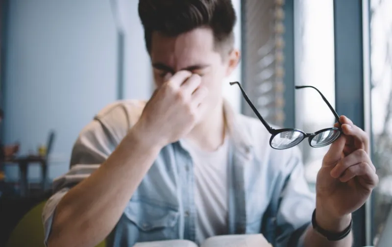 close up portrait of an attractive man with eyeglasses poor young guy has eyesight problems he is rubbing his nose and eyes because of weariness