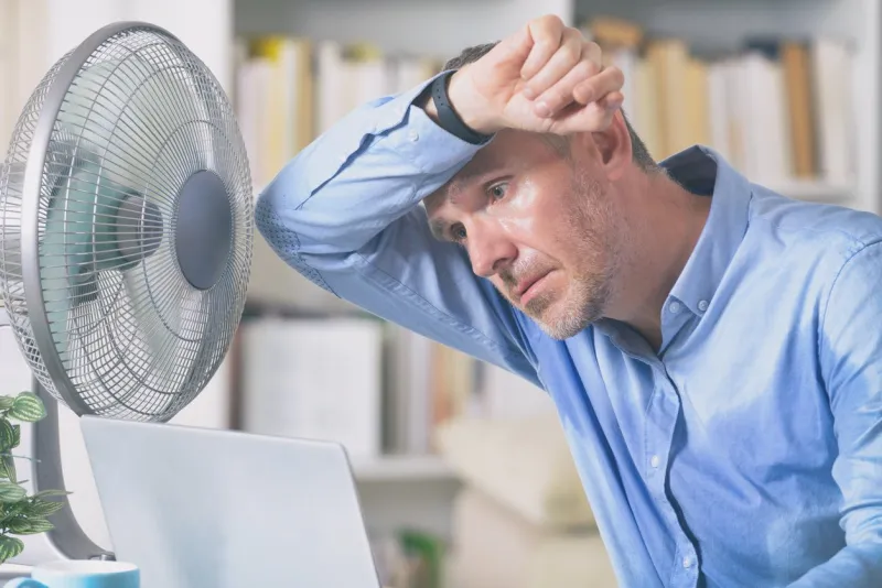 man suffers from heat while working in the office and tries to cool off by the fan