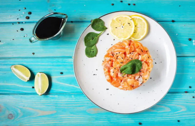delicious avocado and salted salmon tartar on blue wooden background top view