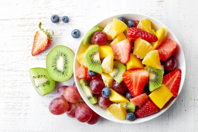 bowl of healthy fresh fruit salad on wooden background top view