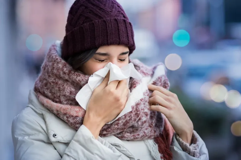 pretty young woman blowing her nose with a tissue outdoor in winter young woman getting sick with flu in a winter day woman with a cold