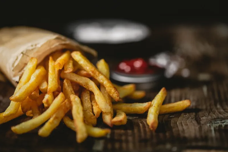 french fries in a basket with ketchup and salt on a dark background