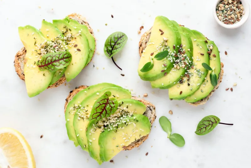 avocado slices with seeds and micro greens on toasted bread on white background healthy vegan vegetarian avocado toasts, top view