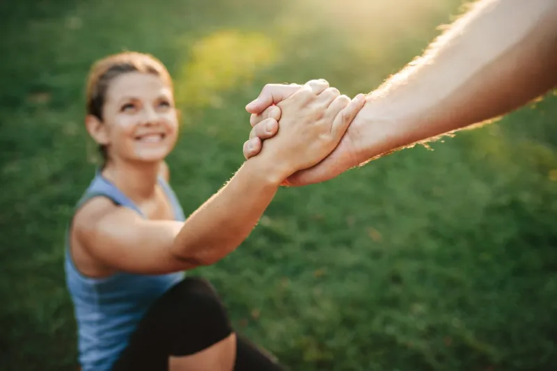 close up shot of man helping woman to stand up focus on hands of couple exercising at park