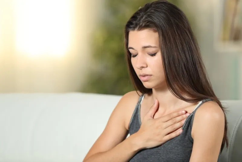 girl having respiration problems touching chest sitting on a couch in the living room at home