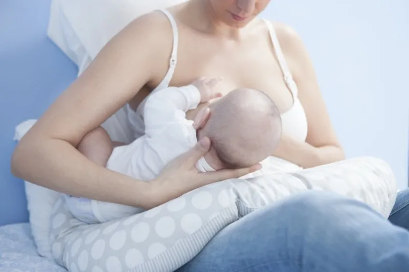 young mother feeding breast she is using a nursing pillow with the baby on side