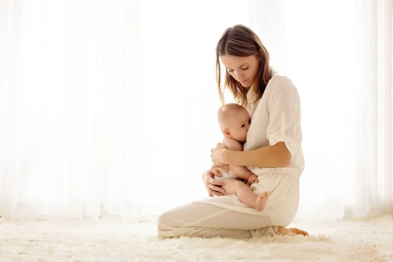 young mother breastfeeding her newborn baby boy at home