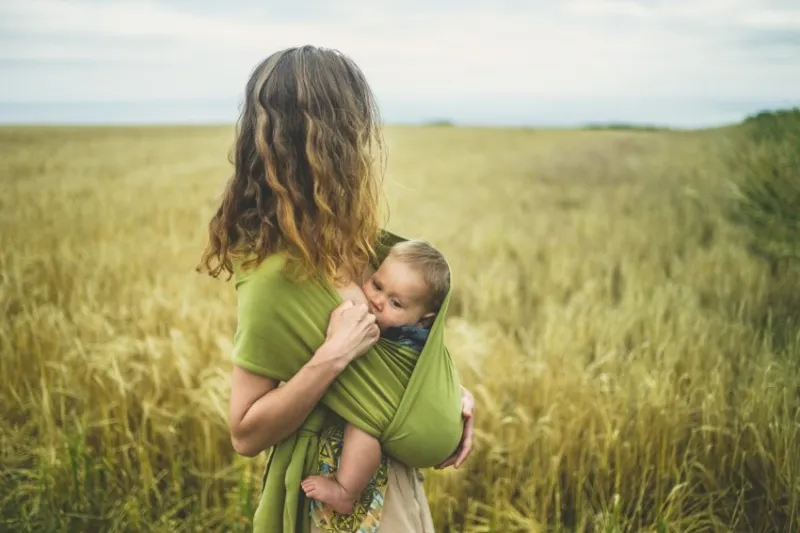 a young mother is breastfeeding her baby in a field