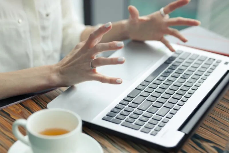 laptop on the table female tense hands with outstretched fingers above the computer white cup of tea next to a laptop stress, irritation