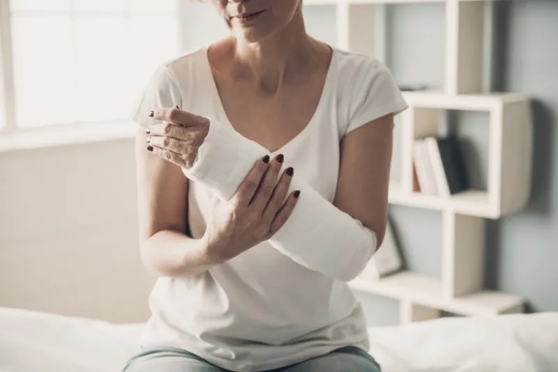 close-up of female broken arm in plaster cast caucasian injured woman in white t-shirt sitting and holding wrist in gypsum bandage with physical pain in fractured bone health care concept