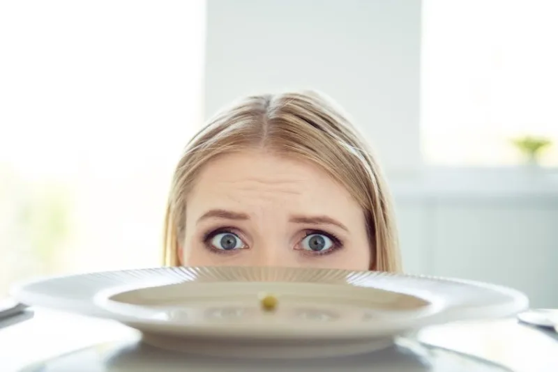 i want to eat many much a lot food cropped close up photo portrait of upset nervous frightened hungry lady looking at camera hiding behind table