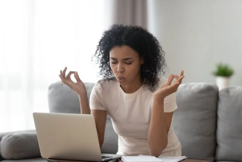 african woman sit on couch near laptop take break reduce stress do yoga meditation exercise to calm down self control get rid of negative emotions, bad e-mail, difficult task, problems at work concept