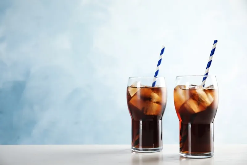 glasses of refreshing cola with ice cubes and straws on table space for text