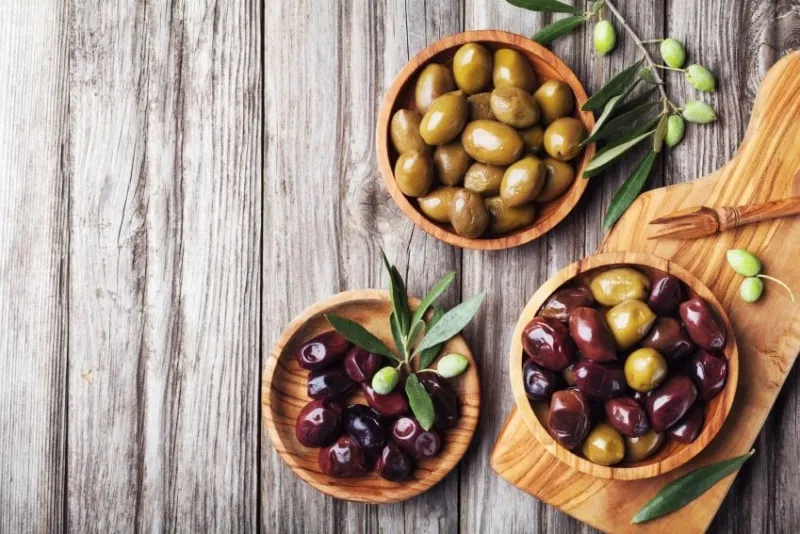 pickled olives served in bowls from olive wood on rustic kitchen table top view