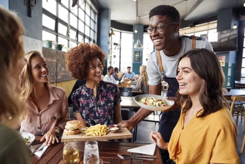 waiter serving group of female friends meeting for drinks and food in restaurant