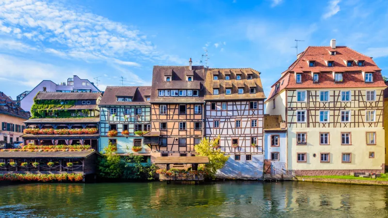 panoramic front view of typical half-timbered buildings with pastel facades lining the river ill in the petite france quarter in strasbourg, france, on a sunny morning
