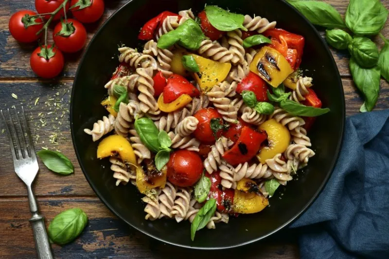 whole wheat fusilli pasta with grilled vegetables in a black bowl on a wooden background top view with copy space