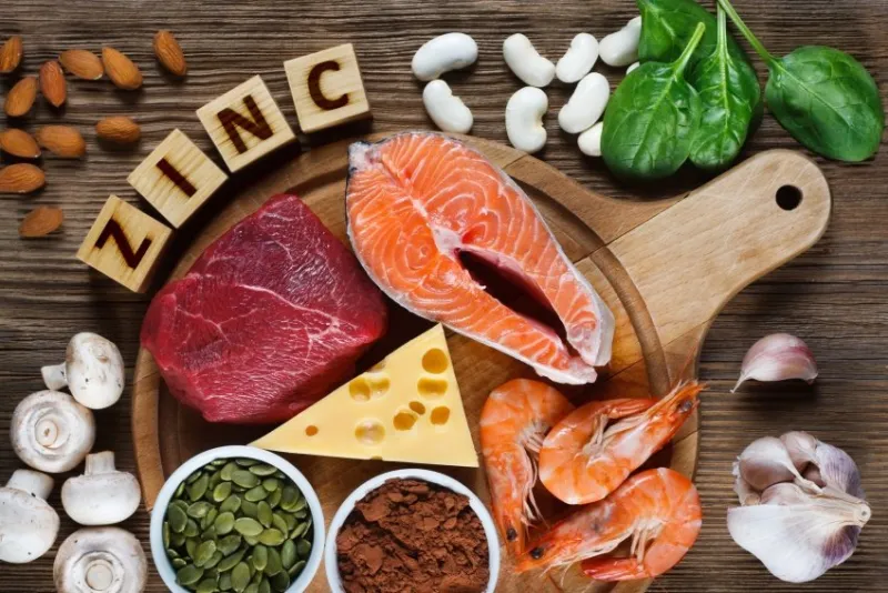 foods high in zinc as salmon, seafood-shrimps, beef, yellow cheese, spinach, mushrooms, cocoa, pumpkin seeds, garlic, bean and almonds top view