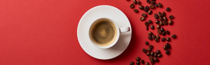 top view of delicious coffee in cup near roasted beans on red background, panoramic shot