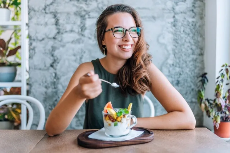 young cheerful woman eating fruit salad