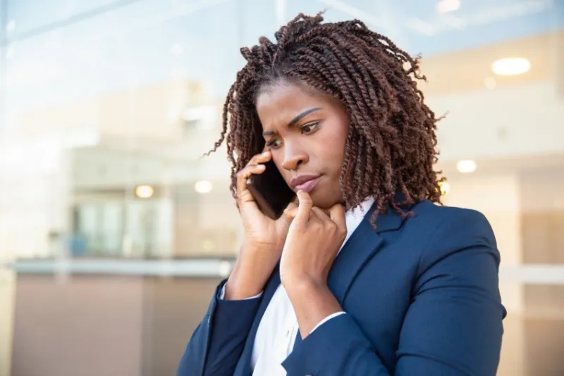 frowning concerned manager speaking on cellphone outside young african american business woman standing near outdoor glass wall mobile phone talk concept