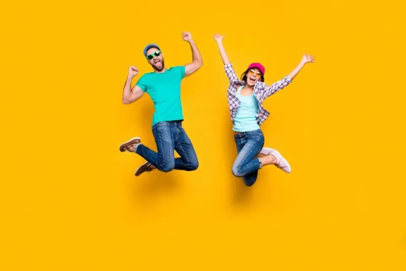 portrait of lucky successful couple jumping with raised fists celebrating victory wearing denim outfit isolated on bright yellow background energy luck success concept