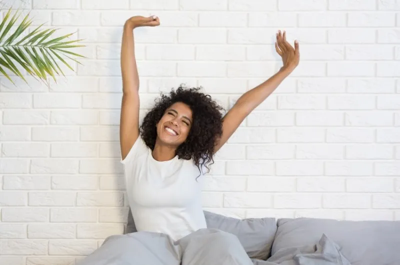beautiful african-american woman waking up in her bed, smiling and stretching, copy space
