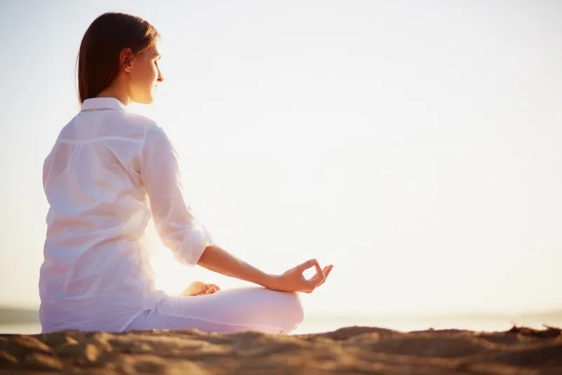 tranquil scene of young female sitting in pose of lotus on the beach in the morning