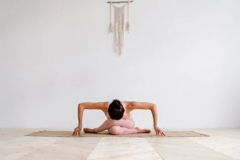 young attractive woman practicing yoga in bright yoga class on wooden vintage floor, sitting in variation of gomukasana exercise with forward bend, cow face pose, working out, wearing pink sportswear