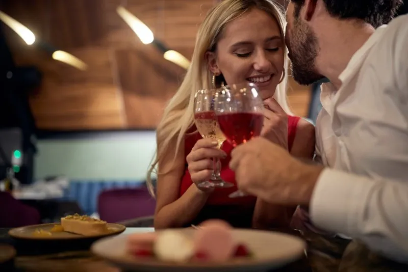 young caucasian man with a beard whispering to attractive blonde at romantic dinner in restaurant