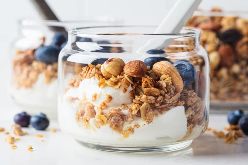 granola with nuts, yogurt and berries in a jar breakfast parfait with muesli, yoghurt and blueberries, white background